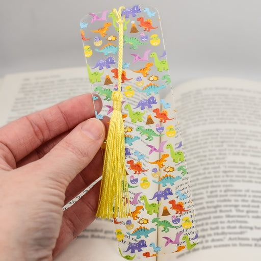 a hand holding a bookmark with dinosaurs on it