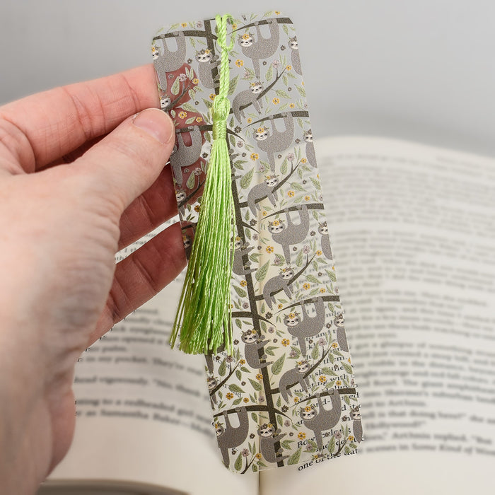 a person is holding a bookmark with a green tassel