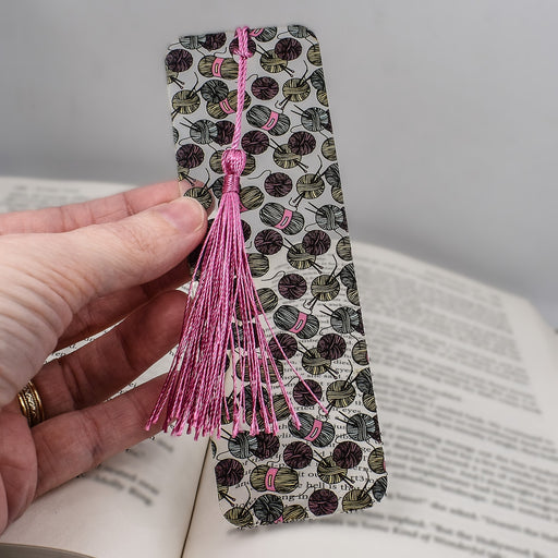 a hand holding a bookmark with a pink tassel