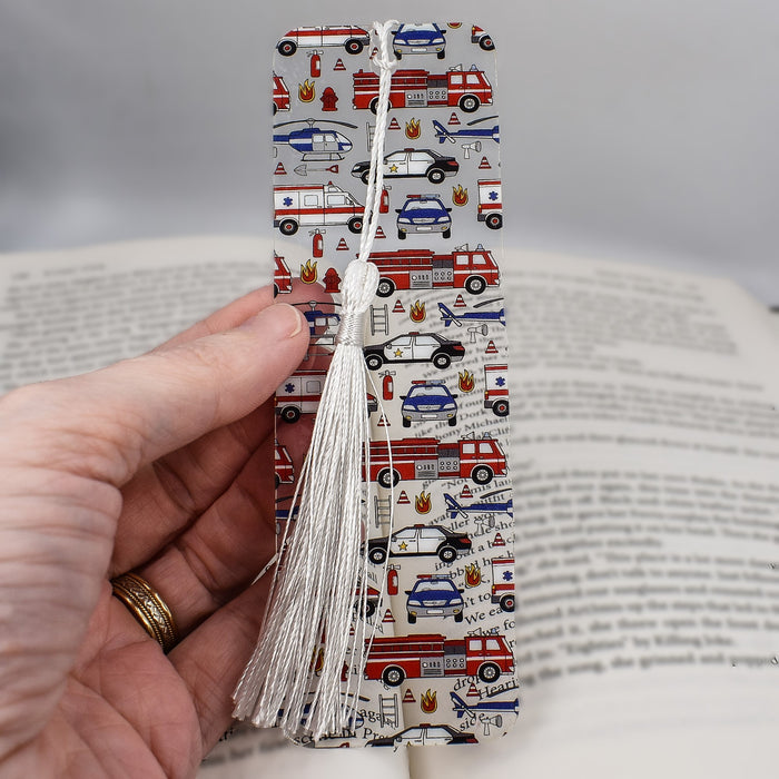 a hand holding a book with a bookmark decorated with cars and trucks