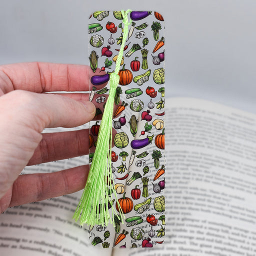 a hand holding a book with a bookmark with vegetables on it