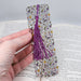 a hand holding a bookmark with a purple tassel