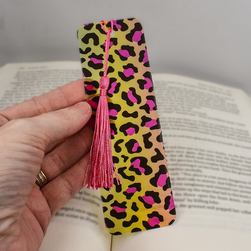 a hand holding a bookmark with a pink tassel