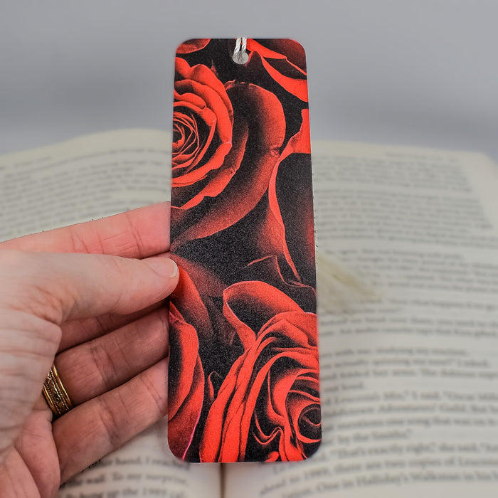 a hand holding a bookmark with red roses on it