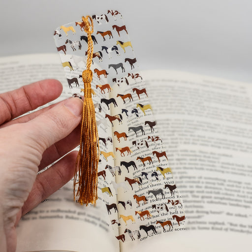a hand holding a bookmark with horses on it