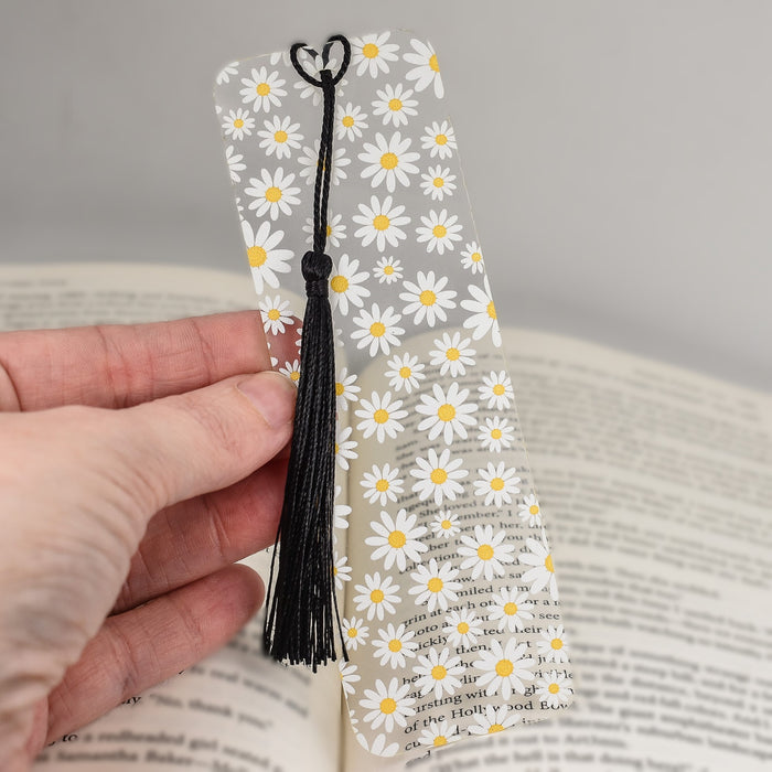 a hand holding a bookmark with daisies on it