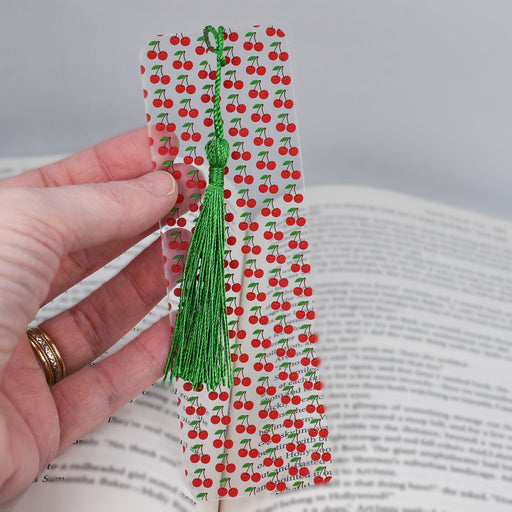 a person is holding a bookmark with a green tassel