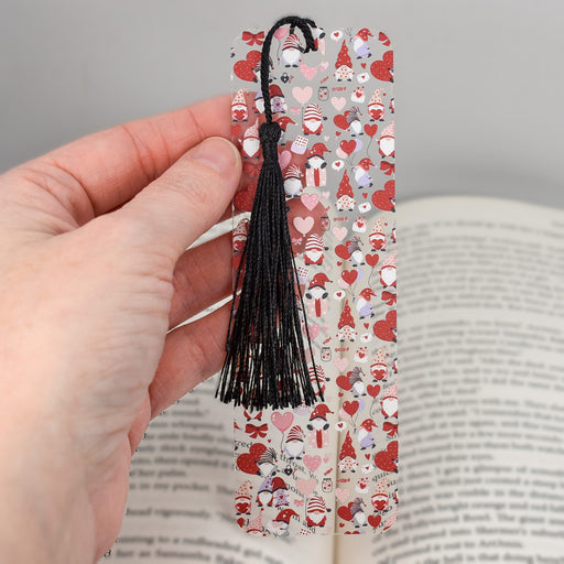 a hand holding a bookmark with hearts and a tassel